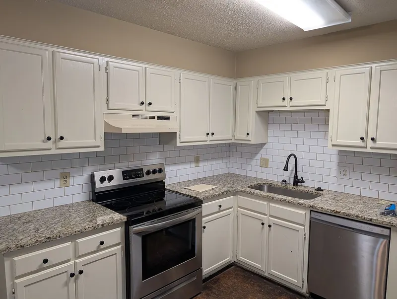Kitchen close-up: white cabinets, granite counters, stainless electric range and dishwasher